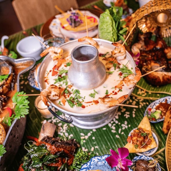 A Thai hot pot with shrimp skewers, surrounded by various dishes on a banana leaf.
