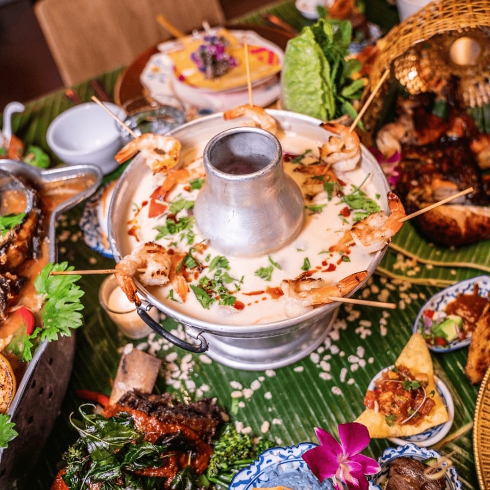 Thai hot pot with shrimp skewers, surrounded by various dishes on a banana leaf.