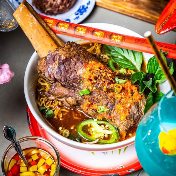 Thai noodle soup with a large beef shank, chili oil, basil, and jalapeños, served with chopsticks.