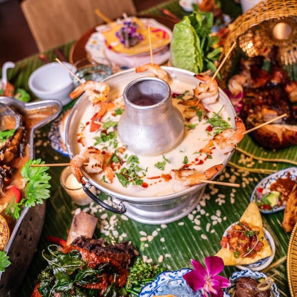 A Thai hot pot with shrimp skewers, surrounded by various Thai dishes on a banana leaf.