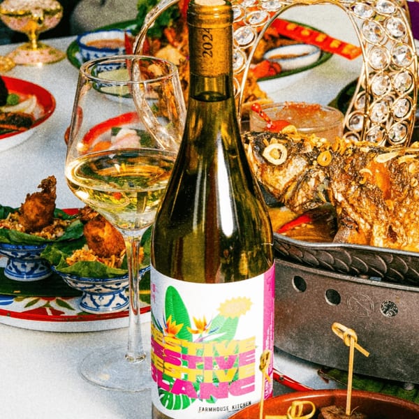 A bottle of Farmhouse Kitchen wine and a glass of white wine on a table with Thai dishes.